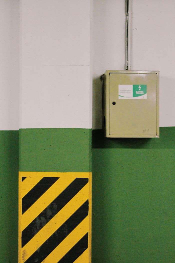 creative-03 Close-up of an electrical box with safety signage and caution stripes on industrial wall.
