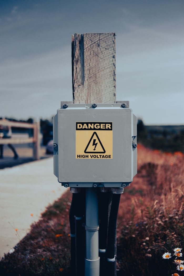 Outdoor electrical box with a high voltage warning sign on a wooden pole.